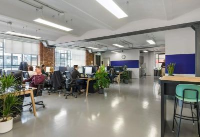 Large open-plan office space with multiple rows of desks, indoor plants, and polished floors.