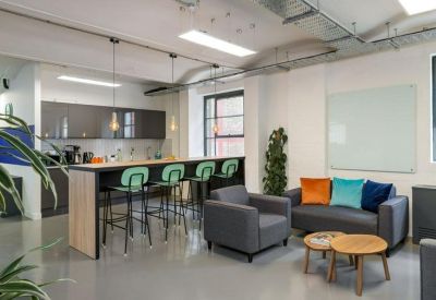 Modern kitchen and breakout area featuring teal bar stools, a grey sofa, and colorful accent pillows.