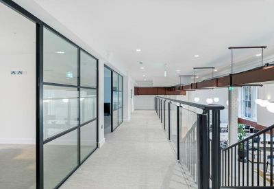 Modern hallway with glass-partitioned offices and a black metal staircase railing.