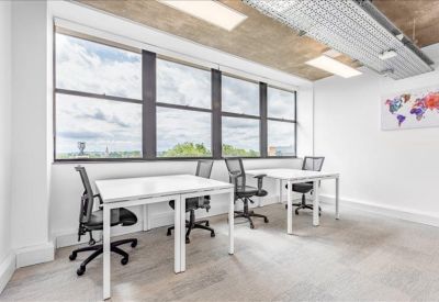 Bright open-plan office space with white desks and black mesh chairs near large windows.