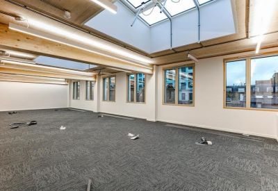 Expansive open-plan office space with grey carpeting, wooden beams, and large windows.