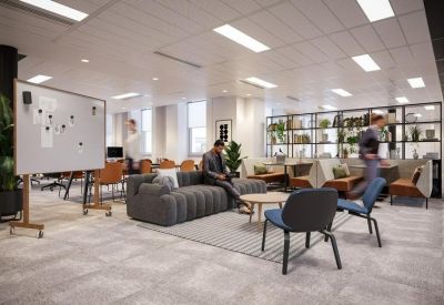 Spacious communal lounge with grey sofas, blue armchairs, and a large whiteboard.
