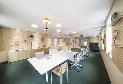 Spacious coworking area with white desks, green carpet, and designer pendant lighting.