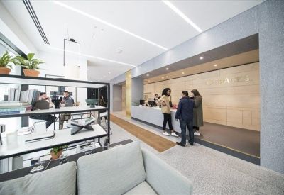 Reception area with a light wood back wall and a sleek white front desk being used by staff.
