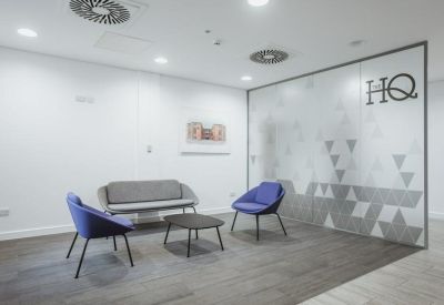 Communal breakout area with blue armchairs, a grey sofa, and a patterned glass partition.