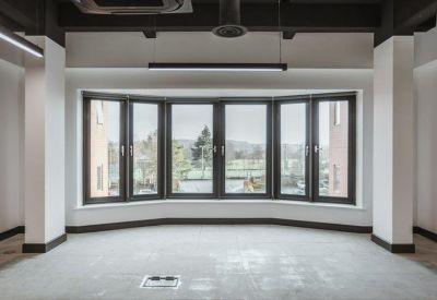 Bright, empty office space with a large five-panel bay window overlooking green space.