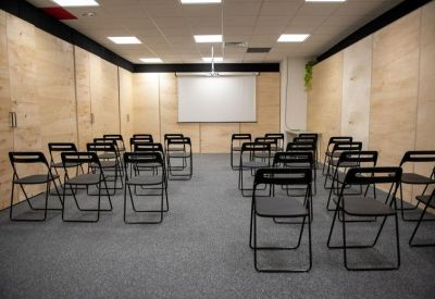 Spacious presentation room with rows of black folding chairs and a projector screen.