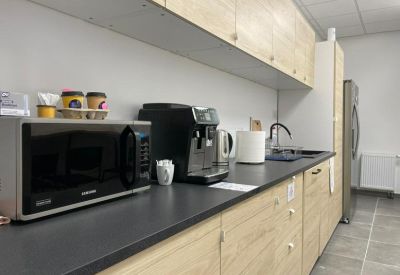 Modern office kitchenette featuring light wood cabinetry, a coffee machine, and black countertops.