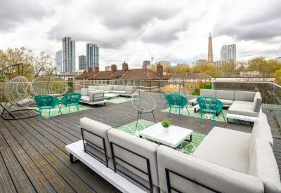 Expansive outdoor roof terrace with various grey sofas and bright turquoise chairs overlooking the city.