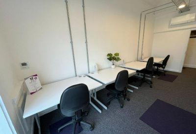 Bright office space with white desks and black ergonomic chairs lined against a white wall.