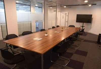 Professional meeting room featuring a long wooden table, black chairs, and a wall-mounted TV screen.