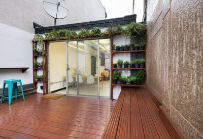 Outdoor terrace with timber decking, a turquoise stool, and a glass door leading into the workspace.