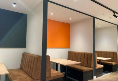 Modern breakout booths with brown leather seating and a vibrant orange feature wall.