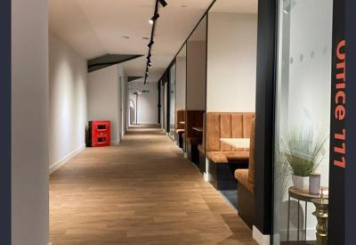 Long bright corridor with glass-fronted offices and warm wood-effect flooring.