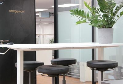 Close-up of a white collaborative standing table with black stools and a potted plant.