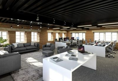 Open-plan office with white desks, grey sofas, and industrial black ceilings.
