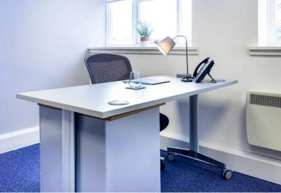Individual workstation with a white desk, ergonomic chair, and desk lamp by a window.