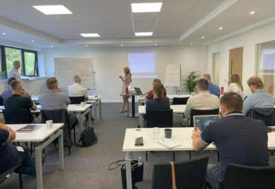 Modern training room with a presenter speaking to a group of people at desks.