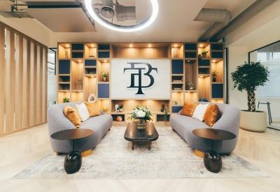Sophisticated reception lounge with grey sofas, a large branded wall, and warm wood shelving.