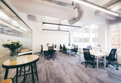 Spacious open-plan office with white desks, black mesh chairs, and large windows.