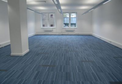 Spacious open-plan office with blue striped carpeting and large windows.