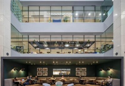 Sunlit multi-story atrium with a dark green seating nook and built-in cafe tables.