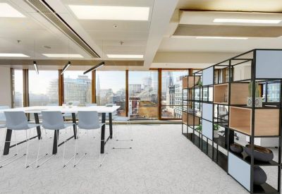 Bright office space with a large white table, light blue chairs, and a black geometric shelving unit.