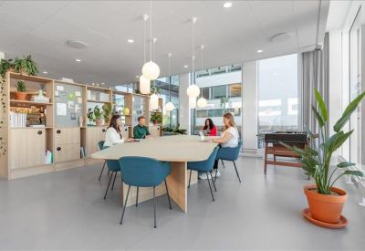 Modern communal area with a large wooden table, blue chairs, and hanging globe lights.