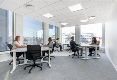Spacious open-plan office with white desks and large windows overlooking the city.