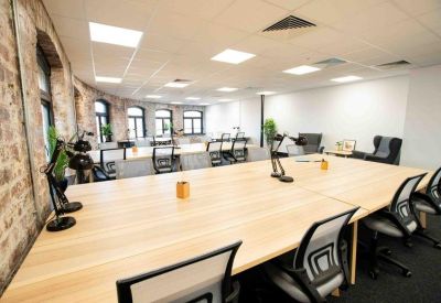 Spacious open-plan coworking area with long wooden desks and large arched windows.