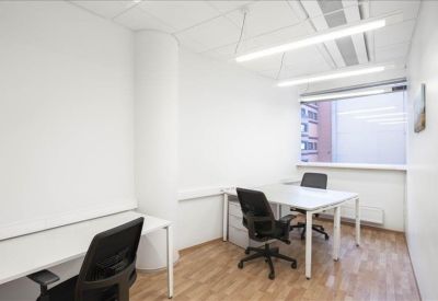 Internal two-person office suite with white desks, black chairs, and wood-laminate flooring.