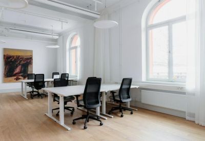 Bright office space with white desks, ergonomic black chairs, and large arched windows.