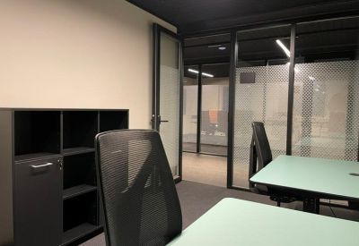 Modern office suite with glass partitions, dark desks, and ergonomic mesh chairs.