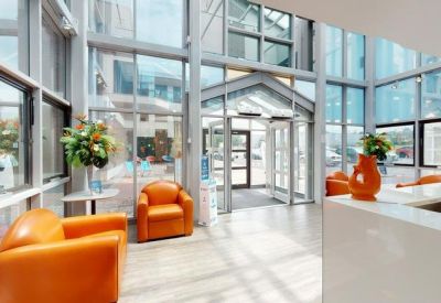 Bright glass-walled lobby with orange armchairs and a white reception desk.