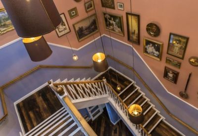 Characterful internal staircase with blue and peach walls decorated with numerous framed artworks.