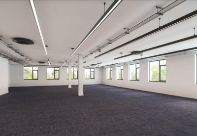 Spacious open-plan office space with dark carpeting and industrial-style ceiling lighting.