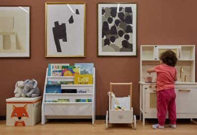 Bright playroom with a child's kitchen set, a small bookshelf, and framed artwork on the wall.