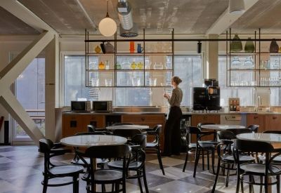 Bright café area with wooden shelving, black bistro chairs, and circular marble-top tables.