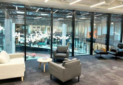 Lounge area with grey armchairs and a view of a large glass-walled interior courtyard.