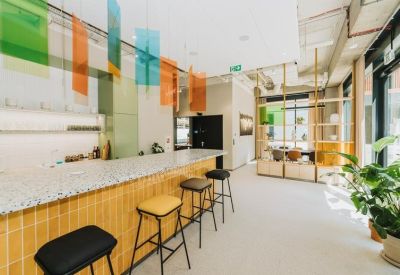 Modern communal cafe area with a yellow tiled counter and colorful hanging panels.