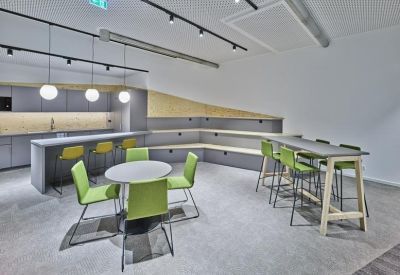 Communal kitchen and breakout area with high-top seating and green accent chairs.