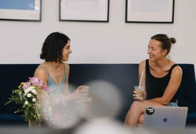 Two people having a casual discussion on a dark blue sofa in a lounge area.