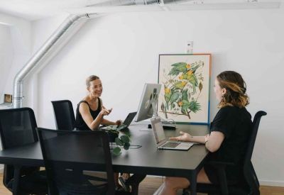 Professional interior with two women working at a large black desk with monitors.