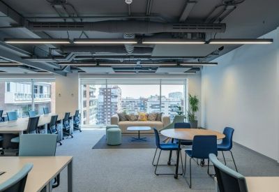 Open-plan office with white desks, blue chairs, and a window overlooking Madrid.