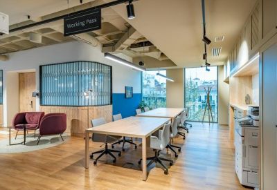 Communal lounge and working area with light wood floors, grey desks, and plush purple armchairs.