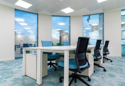 Bright coworking space with white desks, blue office chairs, and large windows.