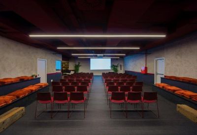 Large presentation room with rows of red chairs and a projector screen.