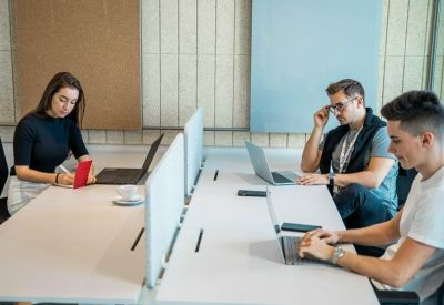 Three people working on laptops at a white desk in a bright office environment.