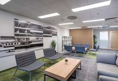 Spacious breakout lounge with grey armchairs, a wooden coffee table, and a large mural wall.