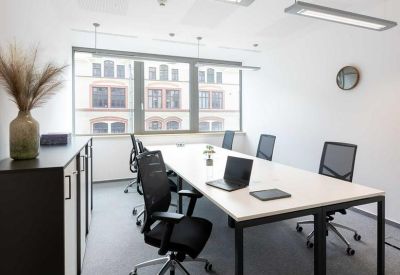 Bright private office featuring a white desk, ergonomic black chairs, and a large window.
